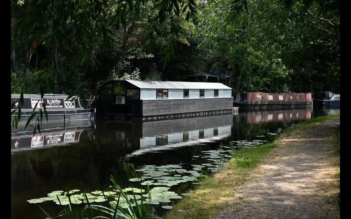 Floating home and narrowboats moored on a tree-lined UK canal